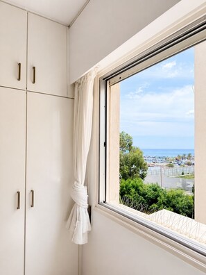 Une pièce avec une fenêtre, un rideau et une vue sur la mer et les bâtiments.
