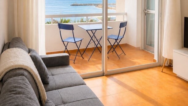 Ein Balkon mit Meerblick, einer Couch und einem Tisch mit Stühlen.