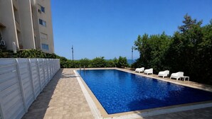 Ein rechteckiger Swimmingpool mit einer gefliesten Liegefläche, umgeben von weißen Liegestühlen und einem weißen Zaun.