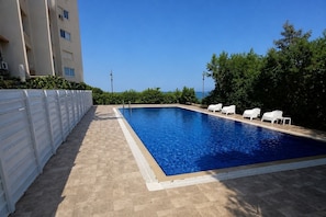 Une piscine rectangulaire avec une terrasse carrelée, entourée de chaises longues blanches et d’une clôture blanche.