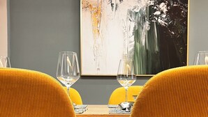 A dining table with two yellow chairs, a glass of wine, and a modern abstract painting on the wall. - Zest Premium Apartments 2 (Durrës)