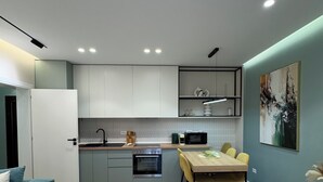 A modern kitchen with built-in appliances, a dining area with a table and chairs, and a living space with a sofa and a coffee table. - Zest Premium Apartments 2 (Durrës)