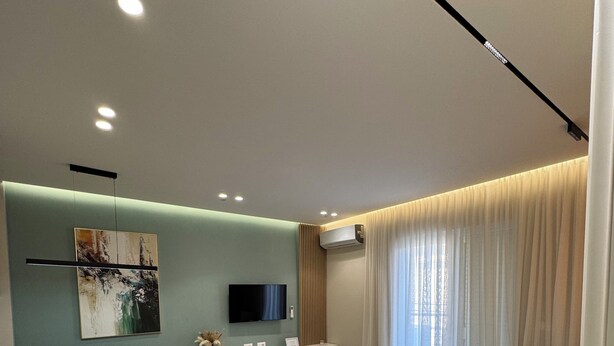 A modern living room with a sofa, dining table, and chairs, a flat-screen TV, and an air conditioning unit. - Zest Premium Apartments 2 (Durrës)