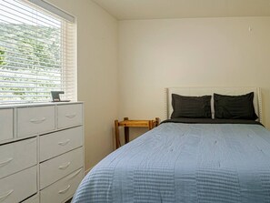 Ein Schlafzimmer mit einem Bett, einem Schminktisch, einem Nachttisch und einem Fenster mit Jalousien.
