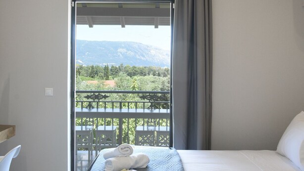A hotel room with a bed, a desk, and a view of a balcony with a mountain landscape.