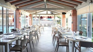 A covered outdoor dining area with tables and chairs, a brick wall, and a view of a pool.