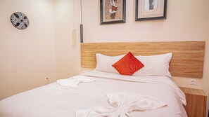 A neatly made bed with white linens and a red pillow, a wooden headboard, and two framed artworks on the wall. - Le Nid Resort (Douala)