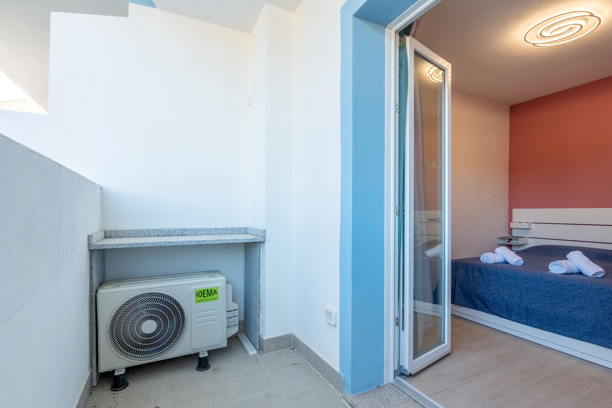 A bedroom with a bed, a sliding glass door, a ceiling fan, and a small air conditioning unit.