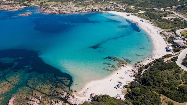 An aerial view of a coastal area with a beach, clear blue waters, and surrounding greenery. - Affittimoderni Trinity D'Agultu - Aquamarine (Trinità d´Agultu e Vignola)