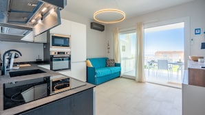 A modern kitchen with built-in appliances, a blue sofa, and a large sliding glass door to an outdoor patio. - Affittimoderni Trinity D'Agultu - Aquamarine (Trinità d´Agultu e Vignola)
