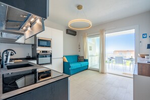 A modern kitchen with built-in appliances, a blue sofa, and a large sliding glass door to an outdoor patio. - Affittimoderni Trinity D'Agultu - Aquamarine (Trinità d´Agultu e Vignola)