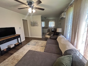A living room with a flat-screen TV, a ceiling fan, a sofa, and a dining area in the background.