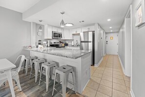 A modern kitchen with a central island, bar stools, a microwave, and a refrigerator. - Seascape Cove at Holiday Towers 605 elevator/pool (Myrtle Beach)