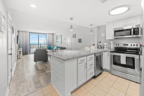 A modern kitchen with a central island, stainless steel appliances, and a view to the outside. - Seascape Cove at Holiday Towers 605 elevator/pool (Myrtle Beach)