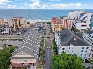 A coastal urban area with a mix of commercial and residential buildings, a parking lot, and a view of the ocean. - Seascape Cove at Holiday Towers 605 elevator/pool (Myrtle Beach)