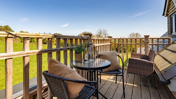 A wooden deck with wicker chairs and a table, a potted plant, and a bottle of wine. - Ferny Retreat -  Romantic barn conversion, Hay-On-Wye (Bromyard)