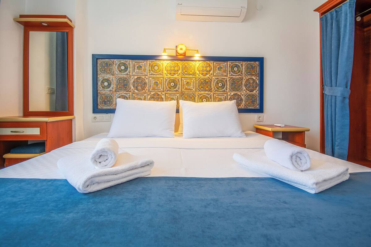 Habitación de hotel con una cama grande, dos almohadas, cabecero con diseño decorativo, mesita de noche y un espejo.