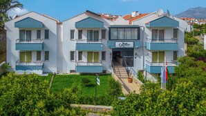 Et hotel med flere etager, altaner, en central indgang og et bjerglandskab i baggrunden.