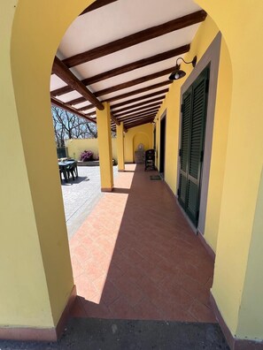 A covered outdoor corridor with yellow walls, a tiled floor, and wooden beams. - La casa di Marina Guest House (Monte Migliore-la Selvotta)