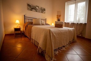 A bedroom with a bed, two bedside tables, a lamp, a painting, and a window with curtains. - La casa di Marina Guest House (Monte Migliore-la Selvotta)