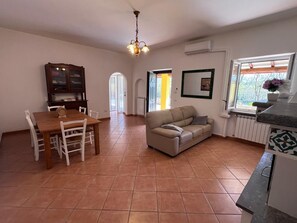 A living room with a sofa, a dining table with chairs, a chandelier, and a window with a view. - La casa di Marina Guest House (Monte Migliore-la Selvotta)