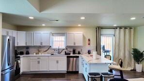 A modern kitchen with white cabinets, stainless steel appliances, a central island, and a view to the outside. - 3-BDR Resort-style Home - Hot Tub, Mini Golf, Fire Pit, Grill, 1Gig WiFi, Office (Richardson)