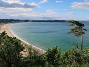 Eine Küstenlandschaft mit sandigem Strand, klarem blauem Wasser und einer Stadt im Hintergrund.