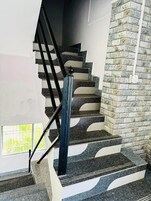 A staircase with alternating black and white steps, a black handrail, and a stone wall on one side.