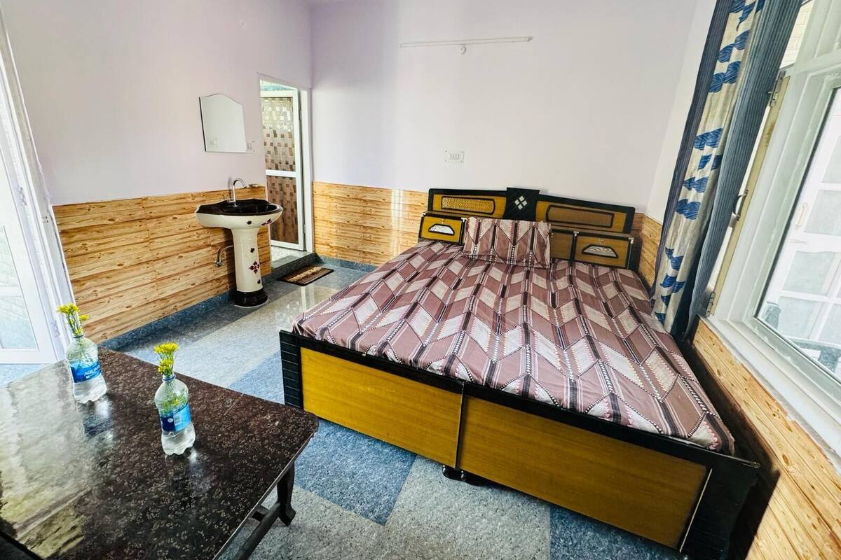 Un dormitorio con cama, mesita de noche con botellas de agua, lavabo y ventana con cortinas.