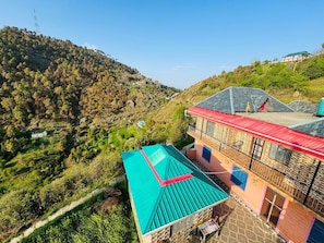 Um edifício em encosta com telhado vermelho e telhado verde, com vista para as colinas arborizadas ao redor.