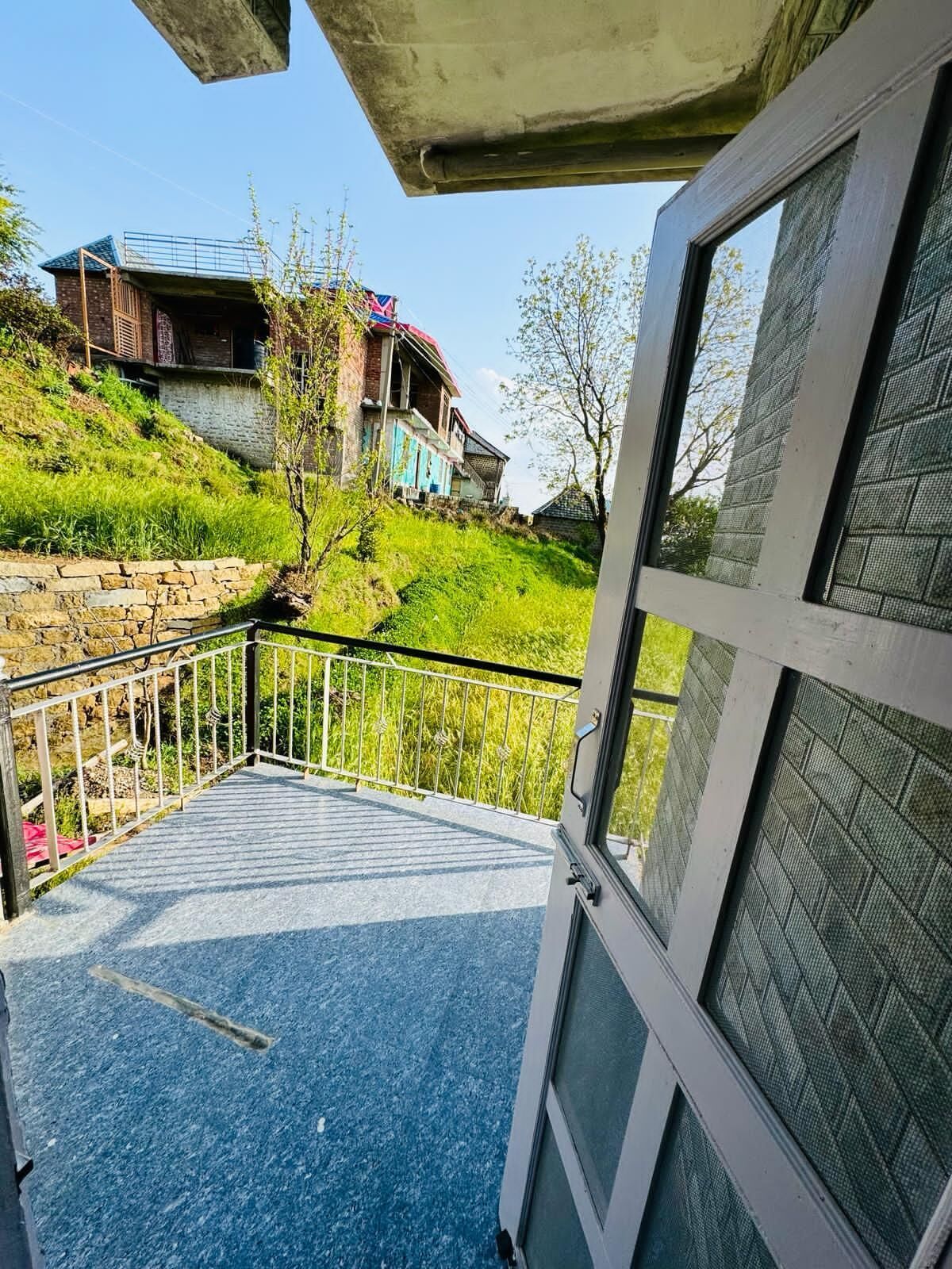 A balcony with a stone wall, a metal railing, and a view of houses on a hillside.