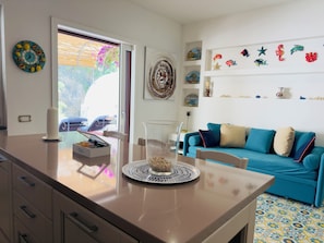 A modern kitchen with a teal sofa, decorative plates, and a clear glass vase on the counter. - O'Mar e O'Sol (Positano)