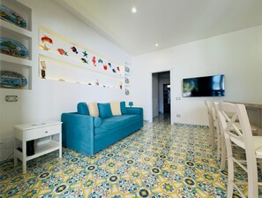 A living room with a blue sofa, a TV mounted on the wall, and a patterned floor. - O'Mar e O'Sol (Positano)