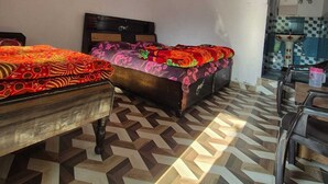 Una habitación con dos camas, piso de baldosas, ventilador, calentador de agua y zona de cocina.
