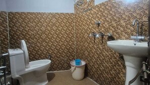 Un baño con inodoro, bidé, lavabo y un equipo de aire acondicionado instalado en la pared.