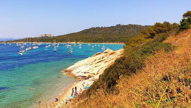 A coastal landscape with clear blue waters, boats, and a rocky shoreline. - Family Escape Steps From the Sea (Hyères)