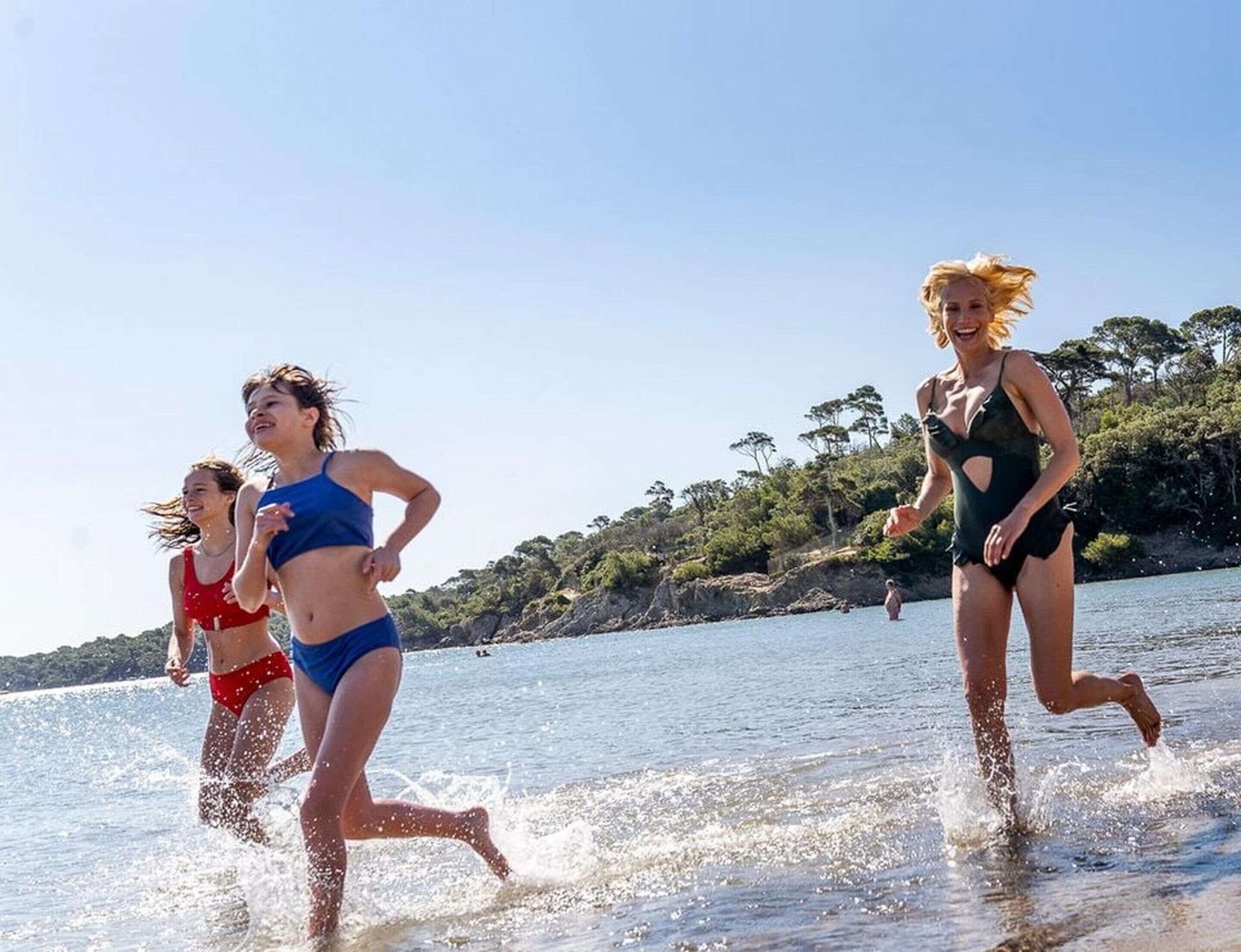 Three individuals running along a beach with water splashing around their feet.