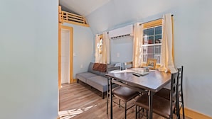 Una habitación con literas, un sofá, una mesa de comedor con sillas y una ventana con cortinas.