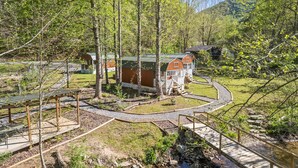 Una cabaña rústica con techo verde, rodeada por un área boscosa con un sendero pavimentado.
