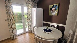 Quarto com uma mesa redonda, cadeiras, um frigorífico e um quadro na parede.