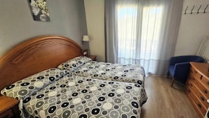 Quarto de hotel com duas camas, uma escrivaninha, uma cadeira, um armário e uma televisão.