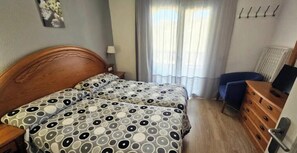 A hotel room with two beds, a desk, a chair, a dresser, and a television. - Jardines del Plaza - Duplex with Garden and Swimming Pools in front of the Sea in Peñíscola (Peníscola)