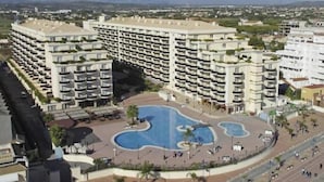 Um hotel grande com várias varandas, uma piscina central e um jardim com palmeiras.