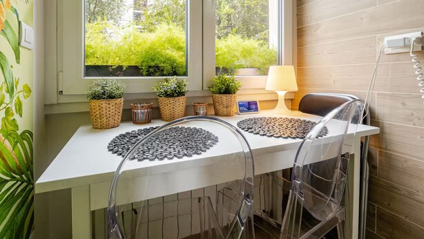 A room with a white desk, clear plastic chairs, a window with a view of greenery and buildings, and a lamp on the desk. - Tropical Chic Flat Near the Centre, 15 minutes to Duomo (Milano)