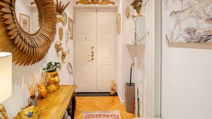 A hallway with a wooden floor, a mirror with a sunburst frame, a door with a gold handle, and a wall with a painting of a leopard. - Tropical Chic Flat Near the Centre, 15 minutes to Duomo (Milano)