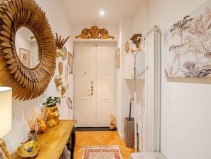 A hallway with a wooden floor, a mirror with a sunburst frame, a door with a gold handle, and a wall with a painting of a leopard. - Tropical Chic Flat Near the Centre, 15 minutes to Duomo (Milano)