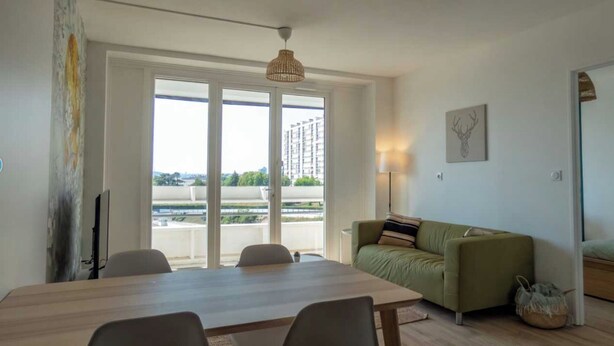 A room with a dining table, chairs, a sofa, a lamp, and a view of a cityscape through large windows. - Private Room in a Shared Apartment - Bron (Bron)