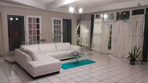 A white sofa, a glass coffee table, and a potted plant in a living room with tiled flooring and a glass door.