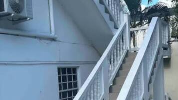 Una escalera conduce a un edificio de fachada blanca, con barandilla metálica y un equipo de aire acondicionado en la pared.