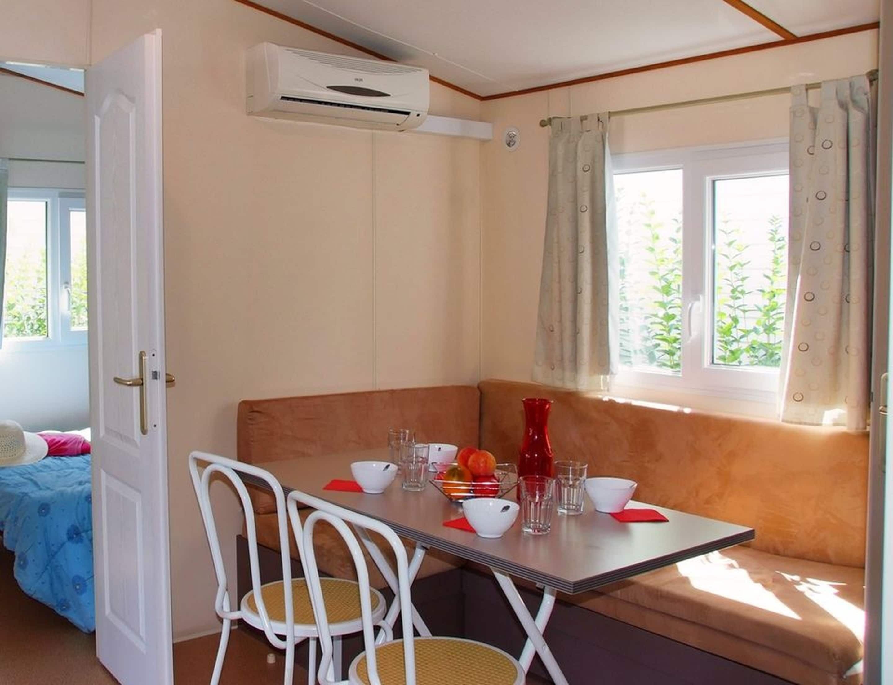 A room with a table set for two, a window with curtains, a door, and an air conditioning unit.